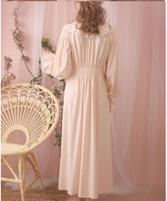 Back view of beautiful standing woman in long, soft Margaret Lawton Nightgown. Cloth covered buttons down the front (not in view) of very feminine pink nightgown with long cuffed poet sleeves and turned down collar trimmed in lace. Partially shirred waist enhances feminine curves. Elegant.