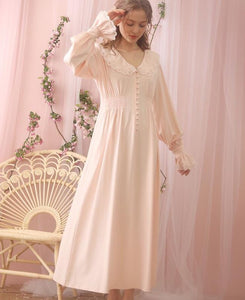 Beautiful standing woman in long, soft Margaret Lawton Nightgown. Cloth covered buttons down the front of very feminine pink nightgown with long cuffed poet sleeves and turned down collar trimmed in lace. Elegant. 