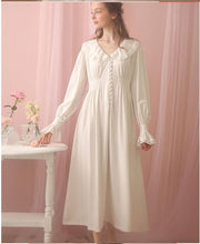 Beautiful standing woman in long, soft Margaret Lawton Nightgown. Cloth covered buttons down the front of very feminine pink nightgown with long cuffed poet sleeves and turned down collar trimmed in lace. Partially shirred waist enhances feminine curves. Elegant.