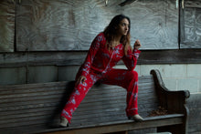 Beautiful woman seated with a leg stretched out wearing richly colored red pajamas with white floral design. These pajamas are made from hand-pulled Peruvian Pima cotton, known for its silky luster and soft hand, combined with modal give the perfect drape, stretch and recovery to these traditional style pajamas by Cat's Pajamas from Margaret Lawton. XS to 2XL
