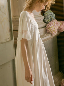 Image of a woman sitting in a chair wearing a Sweet Autumn Vintage Nightgown from Margaret Lawton Nightgowns. Loose fit, small cloth covered buttons and graceful lace short butterfly sleeves. Falls at the knee.