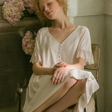 Image of a woman sitting in a chair wearing a Sweet Autumn Vintage Nightgown from Margaret Lawton Nightgowns. Loose fit, small cloth covered buttons and graceful lace short butterfly sleeves. Falls at the knee.